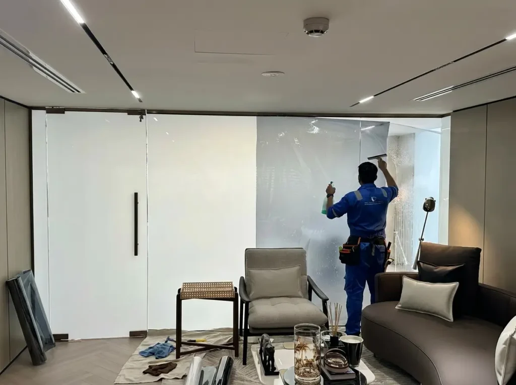 Learn How to Install Smart Glass and Switchable Film? Professional technician installing privacy window film on a large glass window, carefully applying the film in a modern residential or commercial space.